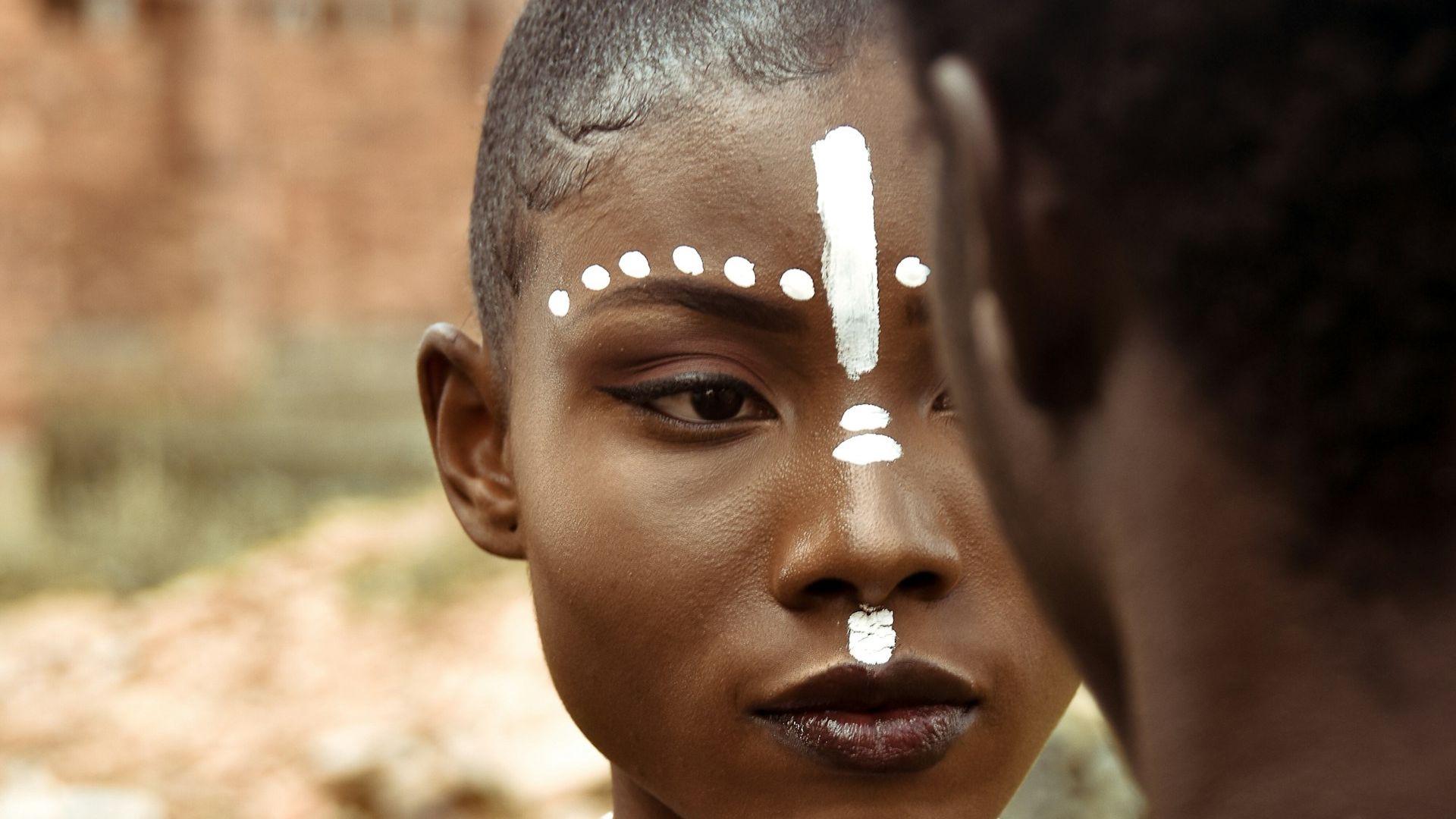 Close-up van een jonge vrouw met traditionele witte gezichtsverf die een andere persoon aankijkt, symbool voor identiteit, expressie en erkenning.